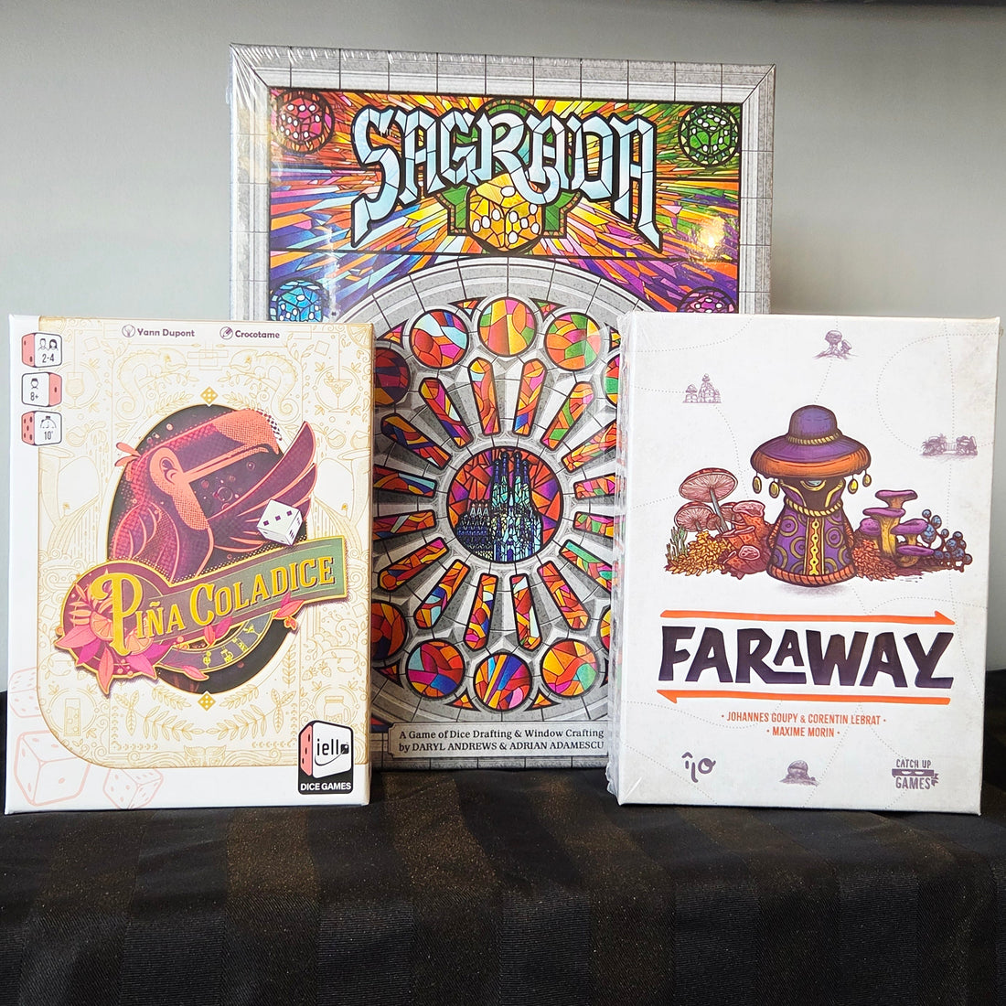 Three board game boxes on a black surface with a plain background